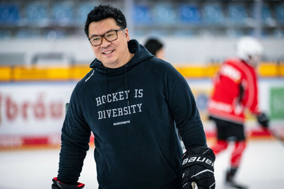 Martin Hyun, schwarze Haare, schwarze Brille, fährt auf dem Eis in einem Stadion. Man sieht den Oberkörper, erträgt einen schwarzen Hoodie mit der Aufschrift "Hockey is Diversity". Er lächelt.